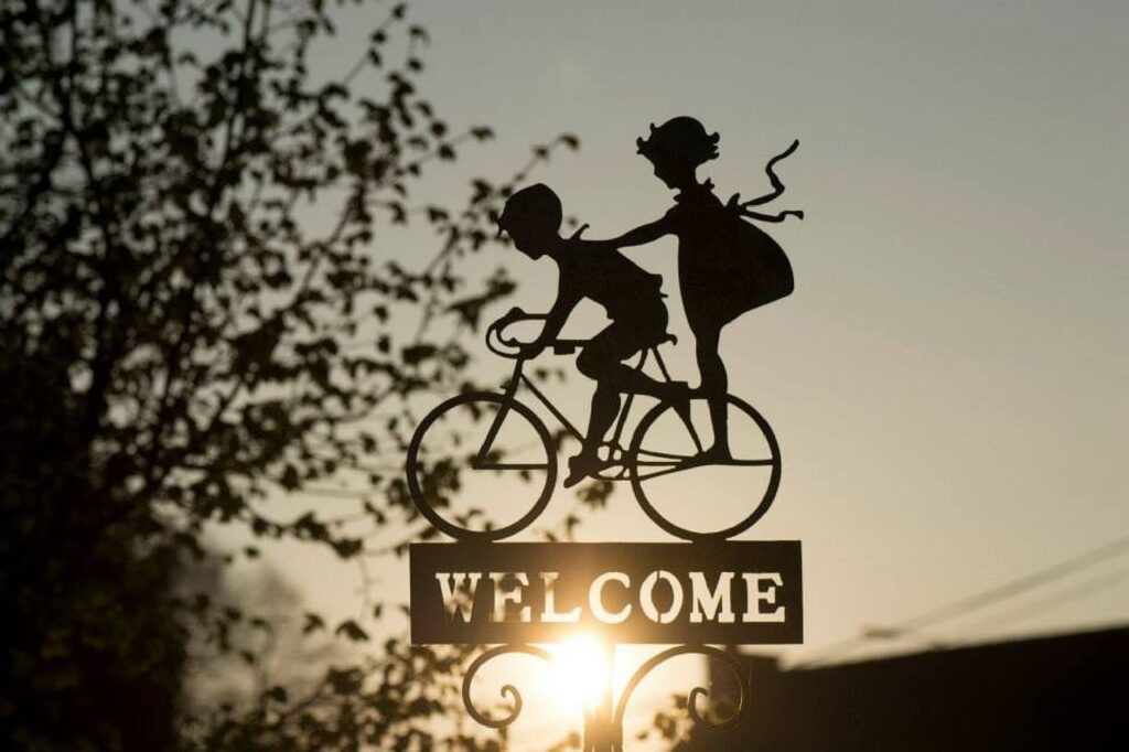 Metal Welcome sign with two kids on a bicycle outside.